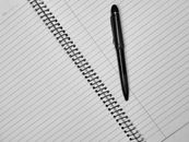 Close-up of a black pen resting on an open spiral notebook with lined pages.