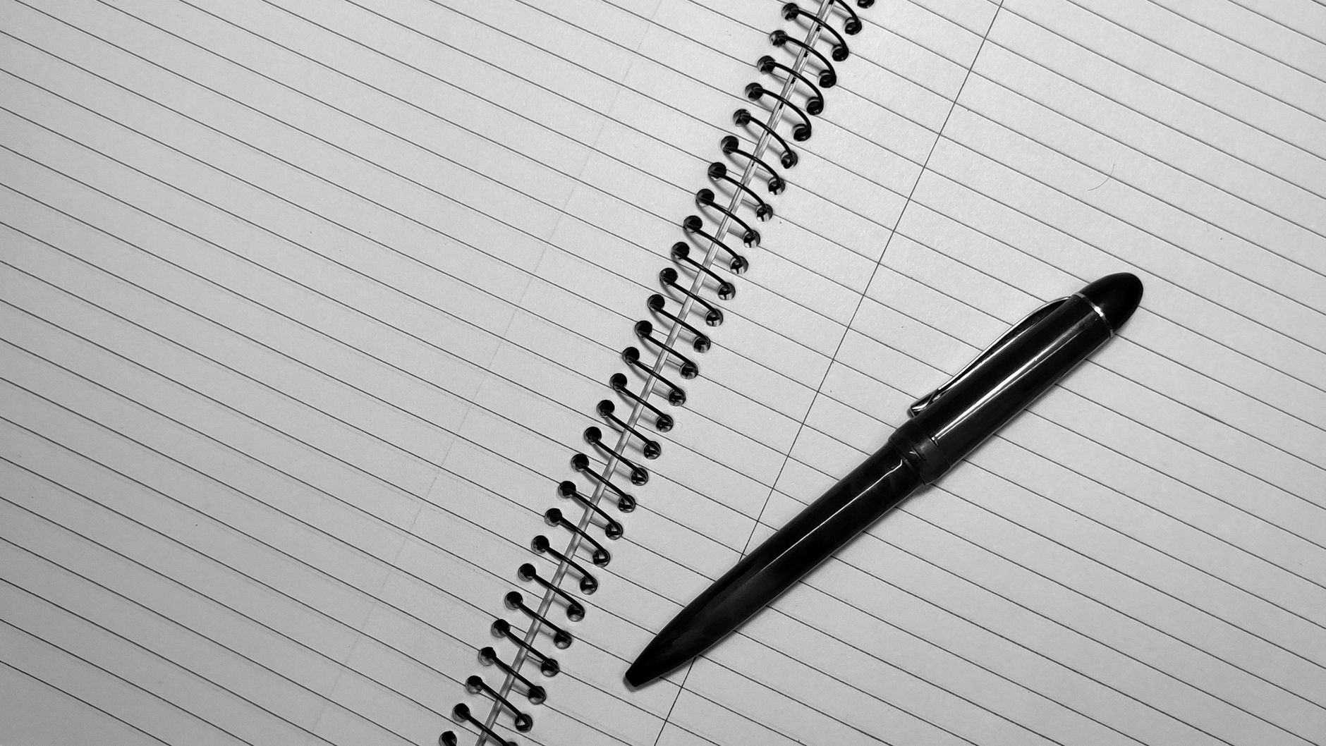Close-up of a spiral notebook with black pen on lined pages, top view.