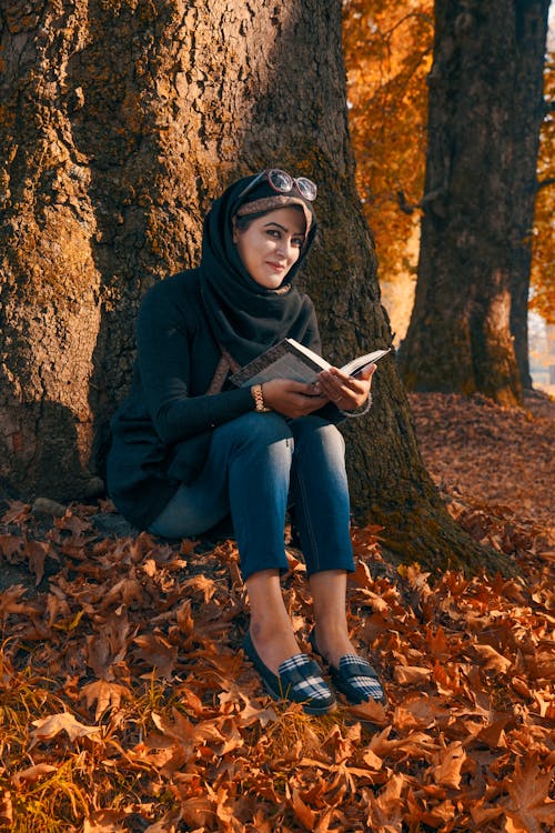 Woman Holding a Book While Sitting on the Ground