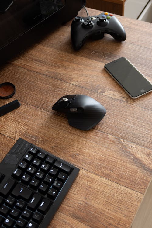 From above arranged black gadgets near keyboard on wooden desk in light room at home