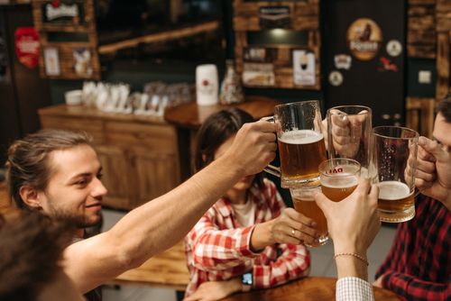 Free Friends celebrate with a toast using beer mugs in a cozy indoor setting. Stock Photo
