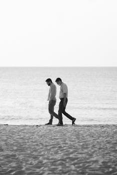 Two men enjoy a peaceful walk along a serene Indonesian beach. Black and white photography captures the moment.