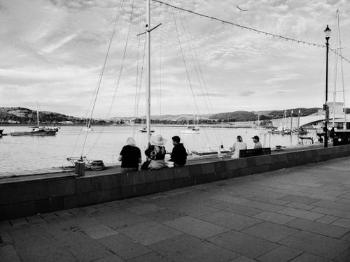 Free People sitting by the seaside with boats in view, creating a peaceful grayscale ambiance. Stock Photo