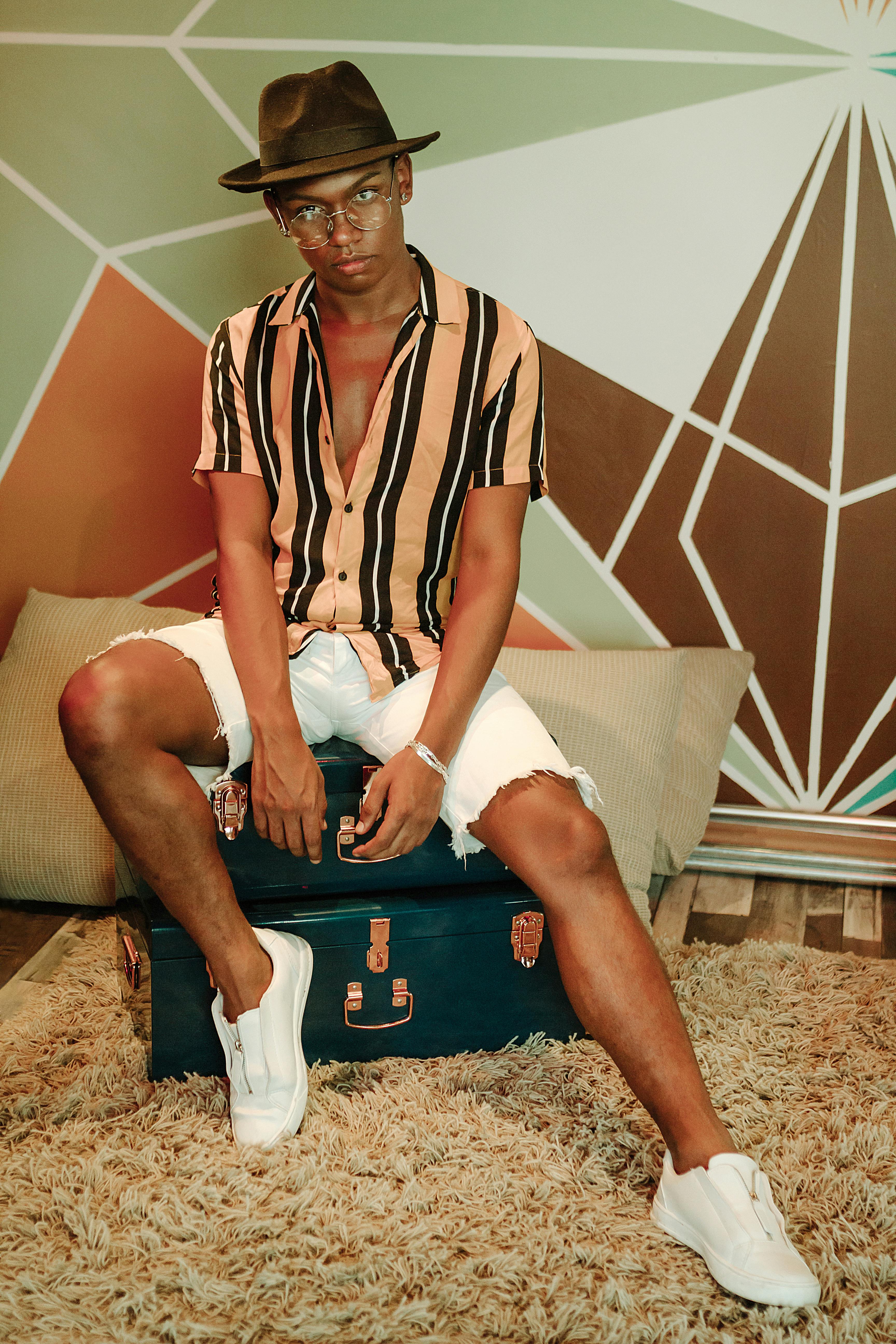 Fashionable young man posing with a brown hat and striped shirt indoors.