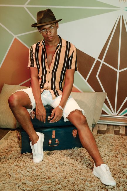 Fashionable young man posing with a brown hat and striped shirt indoors.