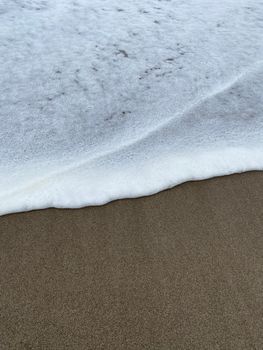 A detailed close-up of gentle waves creating foam on a sandy beach shoreline.