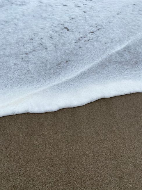 A detailed close-up of gentle waves creating foam on a sandy beach shoreline.