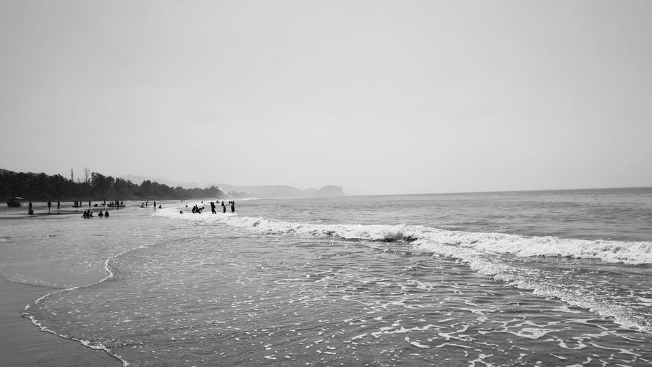 A serene black and white beach scene capturing waves and people enjoying the shore.