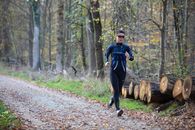 Man in Black and Blue Jacket and Black Pants Walking on Pathway Between Trees