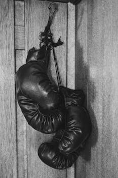 Black and white photo of vintage boxing gloves hanging on a wooden wall, showcasing timeless sports gear.