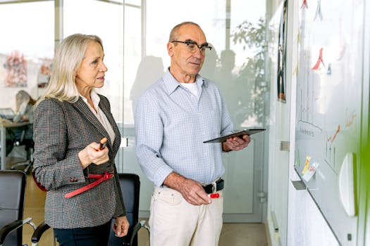 Two professionals engaging in a business meeting, reviewing charts on a whiteboard.