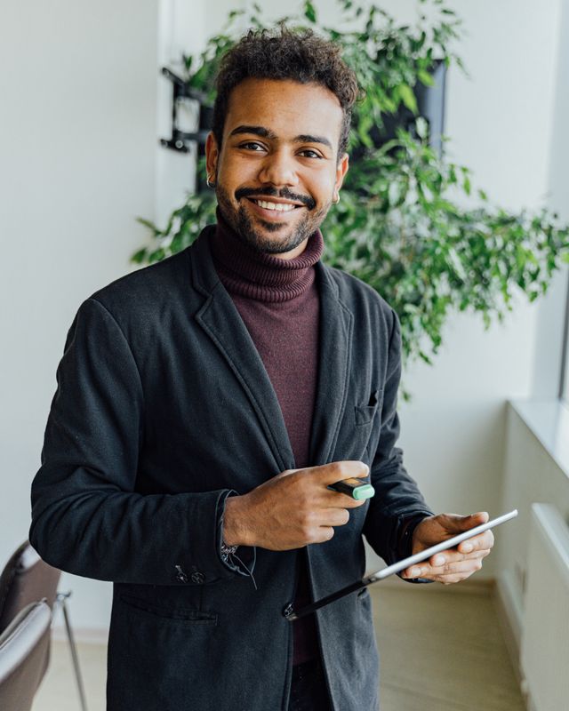 Retrato de um homem de blazer e gola alta, sorrindo, com um tablet na mão.