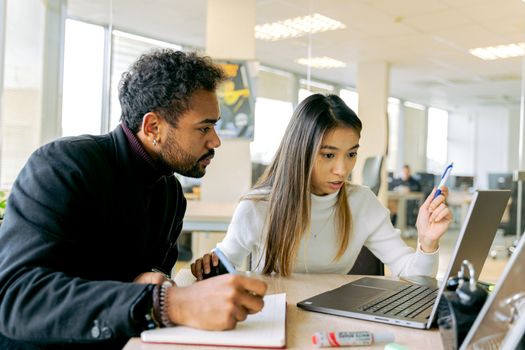 在现代办公室环境中，两位年轻的专业人士正用笔记本电脑讨论工作