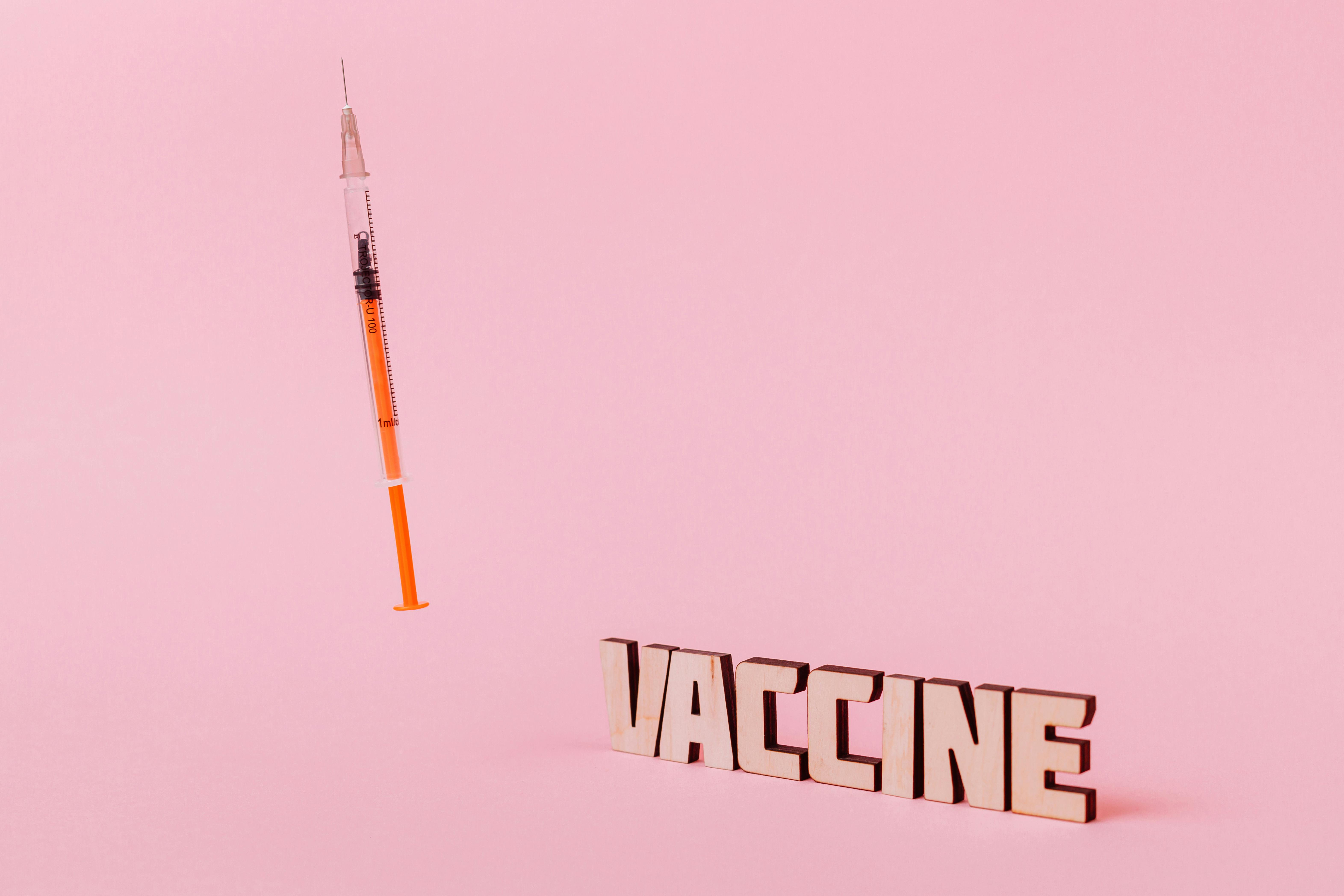 a syringe and vaccine text on pink background