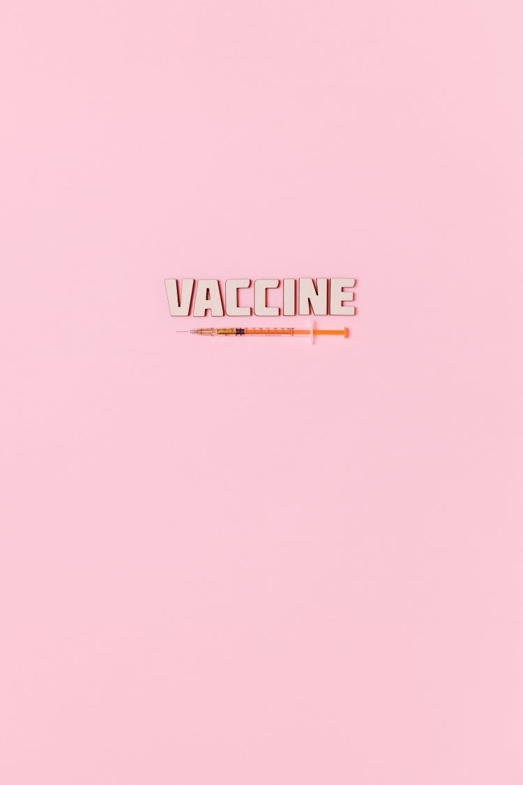 A Syringe And Vaccine Text On Pink Background