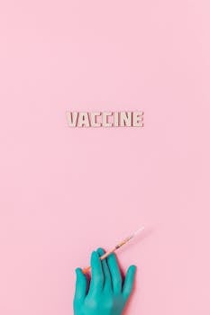A syringe held by a gloved hand with the word 'VACCINE' on a pink background, symbolizing healthcare.