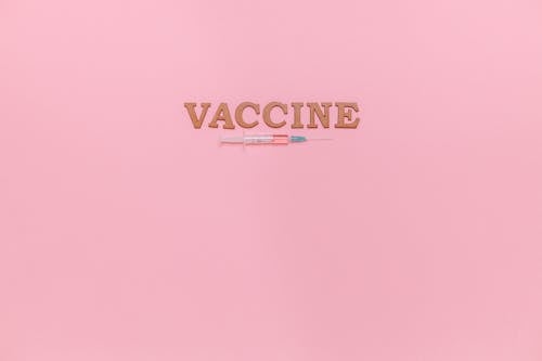 Free A Syringe and Vaccine Text on Pink Background Stock Photo