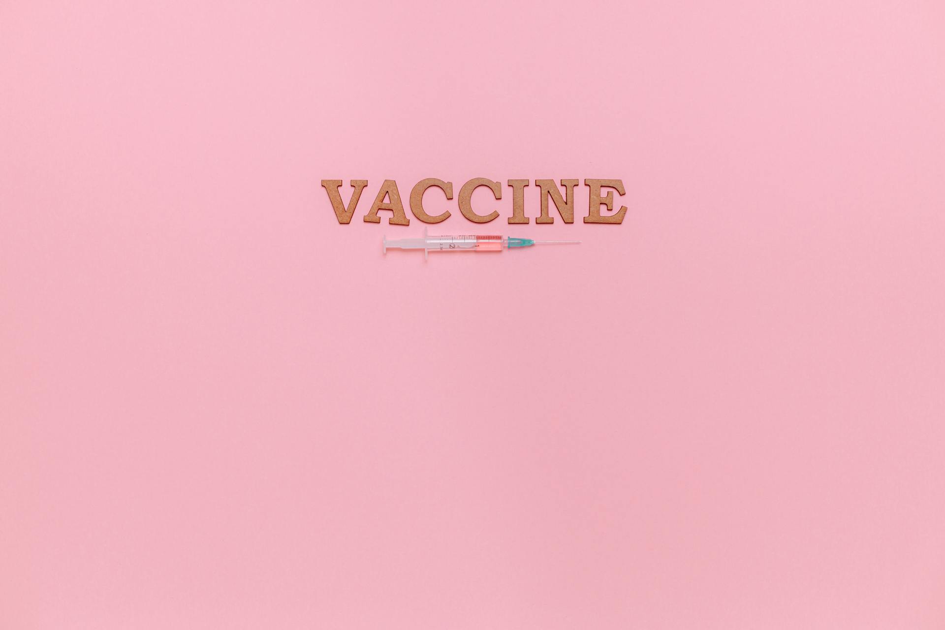 A Syringe and Vaccine Text on Pink Background