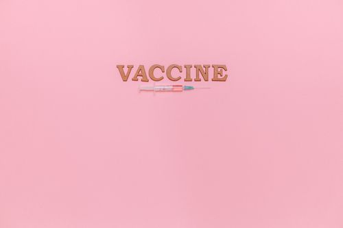 Free A vaccine syringe and word 'VACCINE' on a pink background, ideal for healthcare themes. Stock Photo