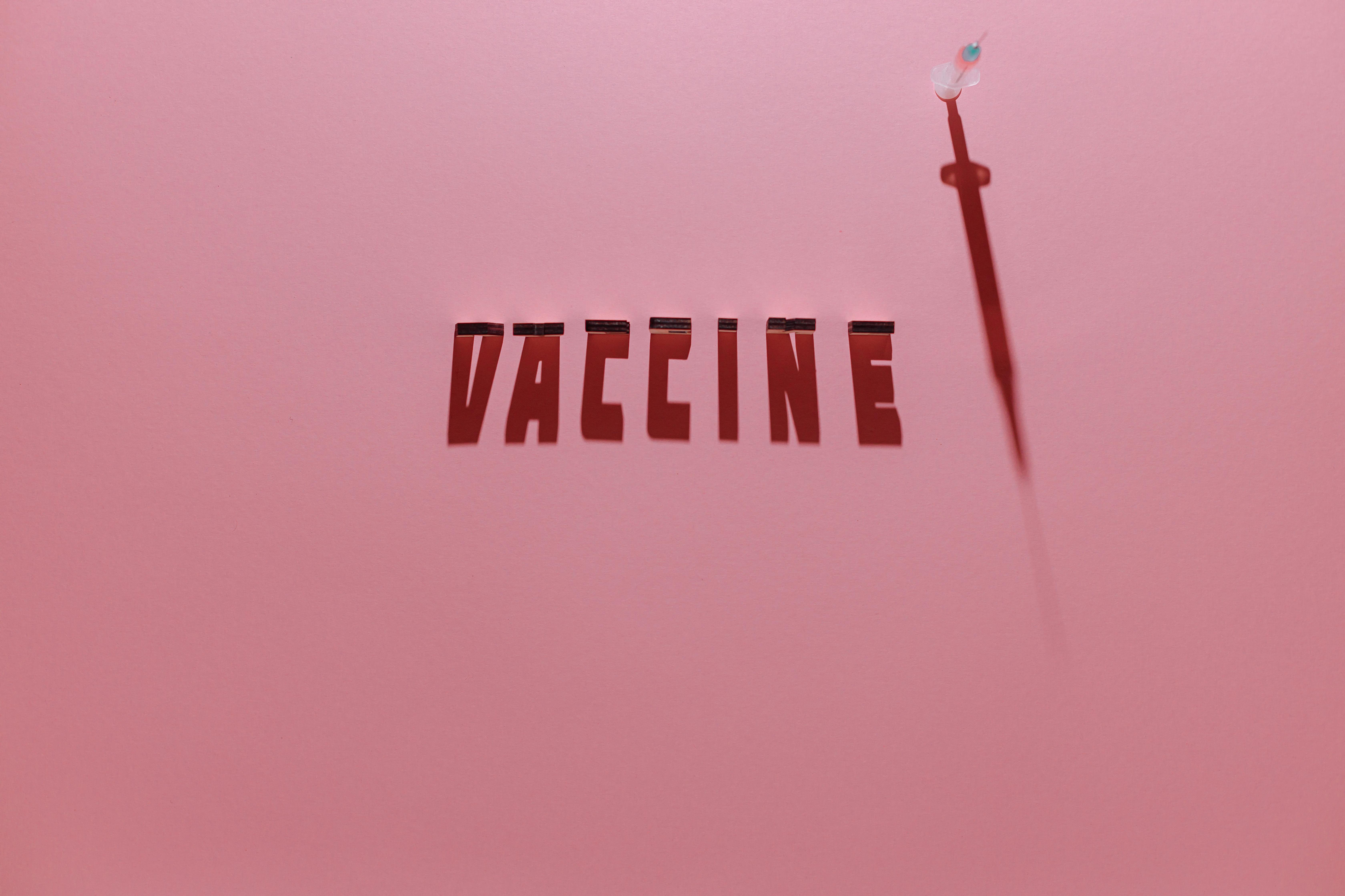 a syringe and vaccine lettering text on pink background