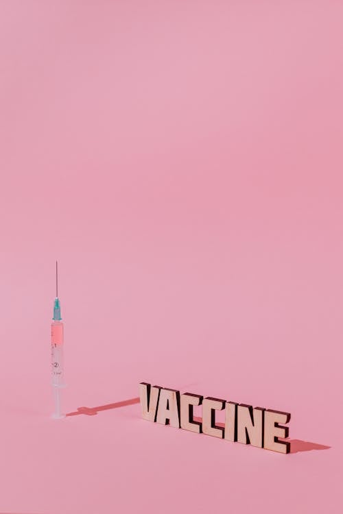 Шприц и текст надписи вакцины на розовом фоне