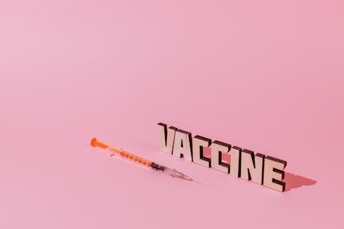 Free A Syringe and Vaccine Lettering Text on Pink Background Stock Photo