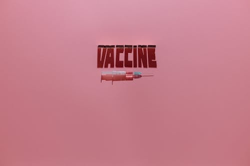 Free A Syringe and Vaccine Lettering Text on Pink Background Stock Photo