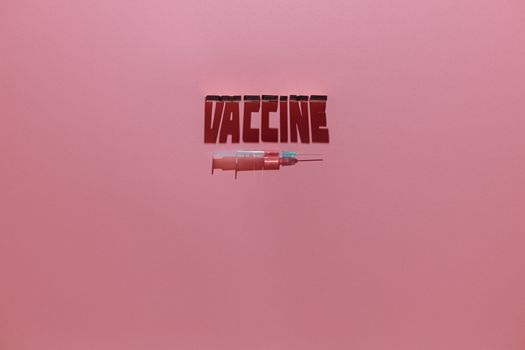 粉红色背景上的注射器和“疫苗”文字象征着医疗保健和免疫