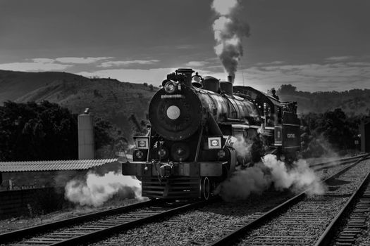 A classic steam locomotive emitting smoke on a scenic railway line with hills in the background., free online jigsaw puzzle on JigsawPuzzlesFreeOnline.org