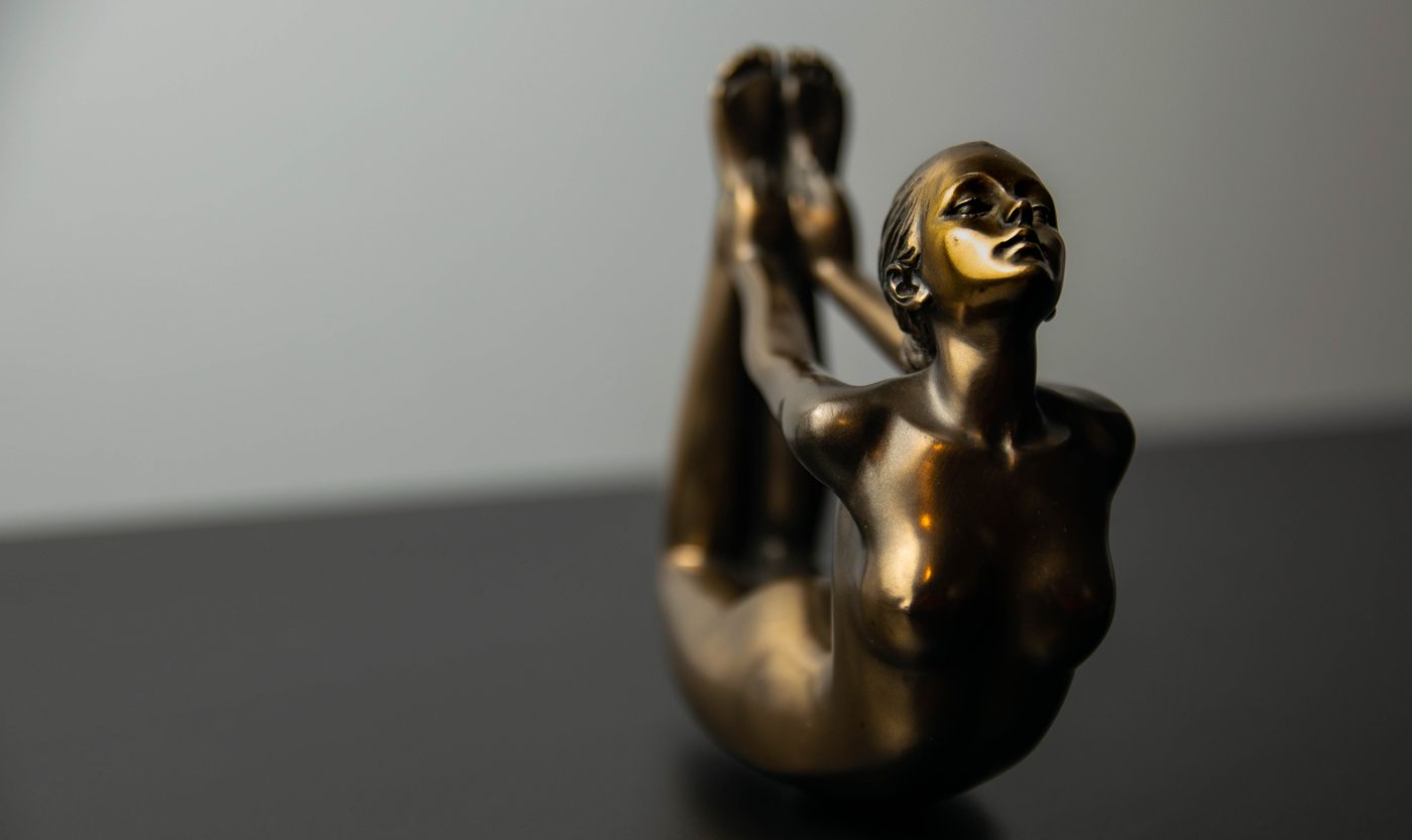 A bronze figure of a stretching woman against a grey wall — photo by Cristian Mihaila on Pexels