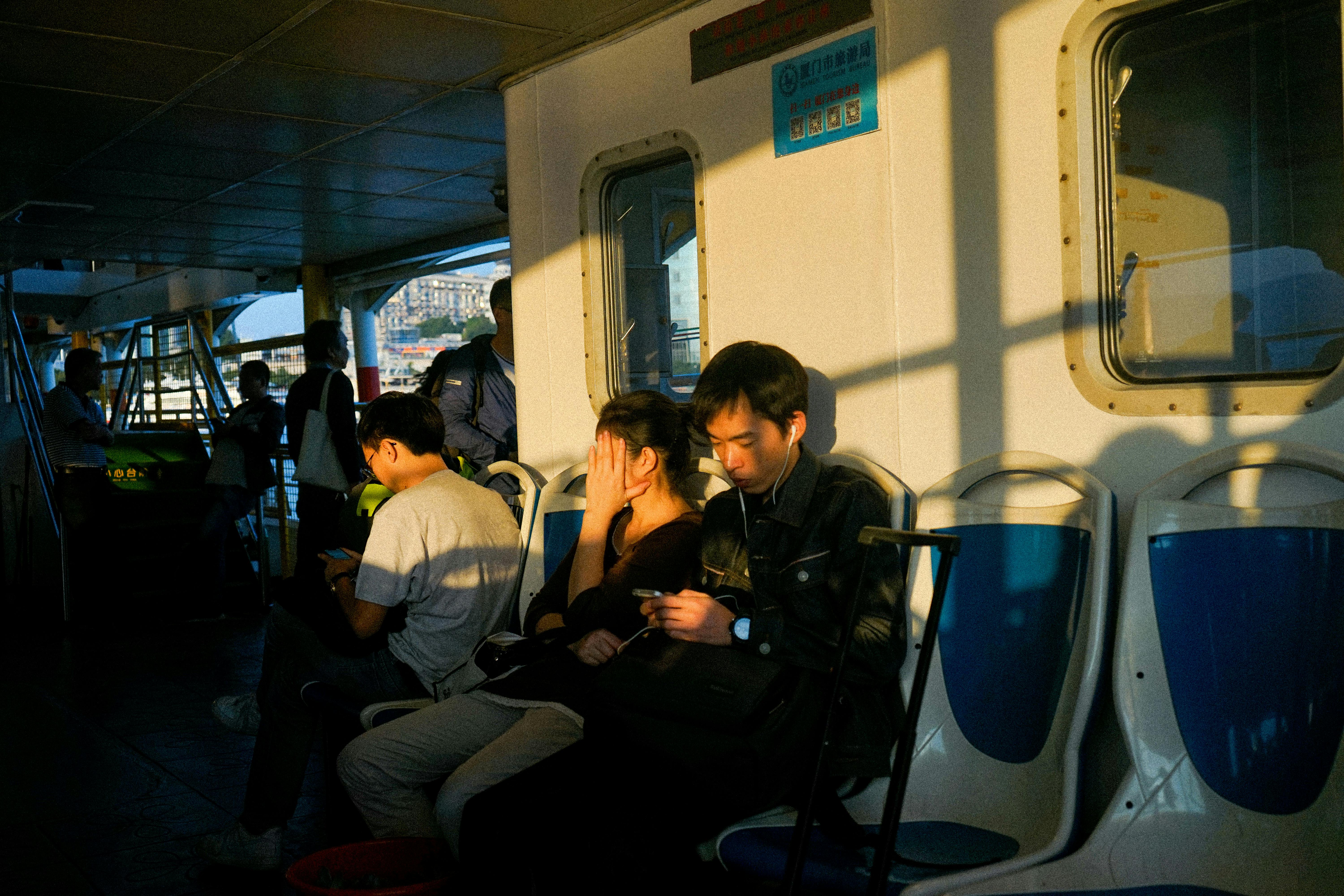 Free Passengers on a ferry engrossed in their devices during twilight, creating a serene travel moment. Stock Photo