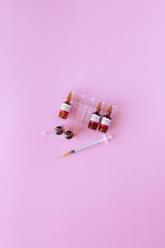 粉红色背景上，医用小瓶和注射器平放，象征着疫苗接种和医疗保健