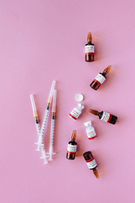 COVID-19 vaccine vials and syringes arranged on a vibrant pink surface.