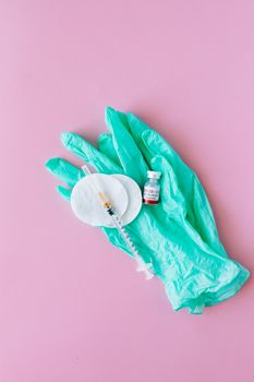 粉色背景上摆放着医用手套、注射器和小瓶
