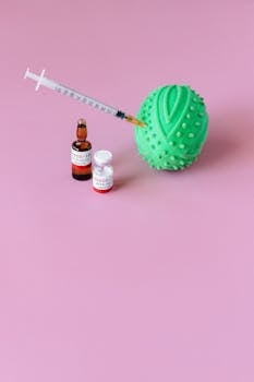 Colorful composition of COVID-19 vaccine with syringe and stress ball against a pink backdrop.