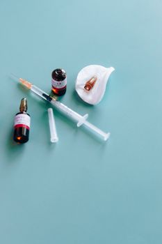 青色背景下，医用注射器、小瓶和安瓶的特写展示了医疗保健必需品