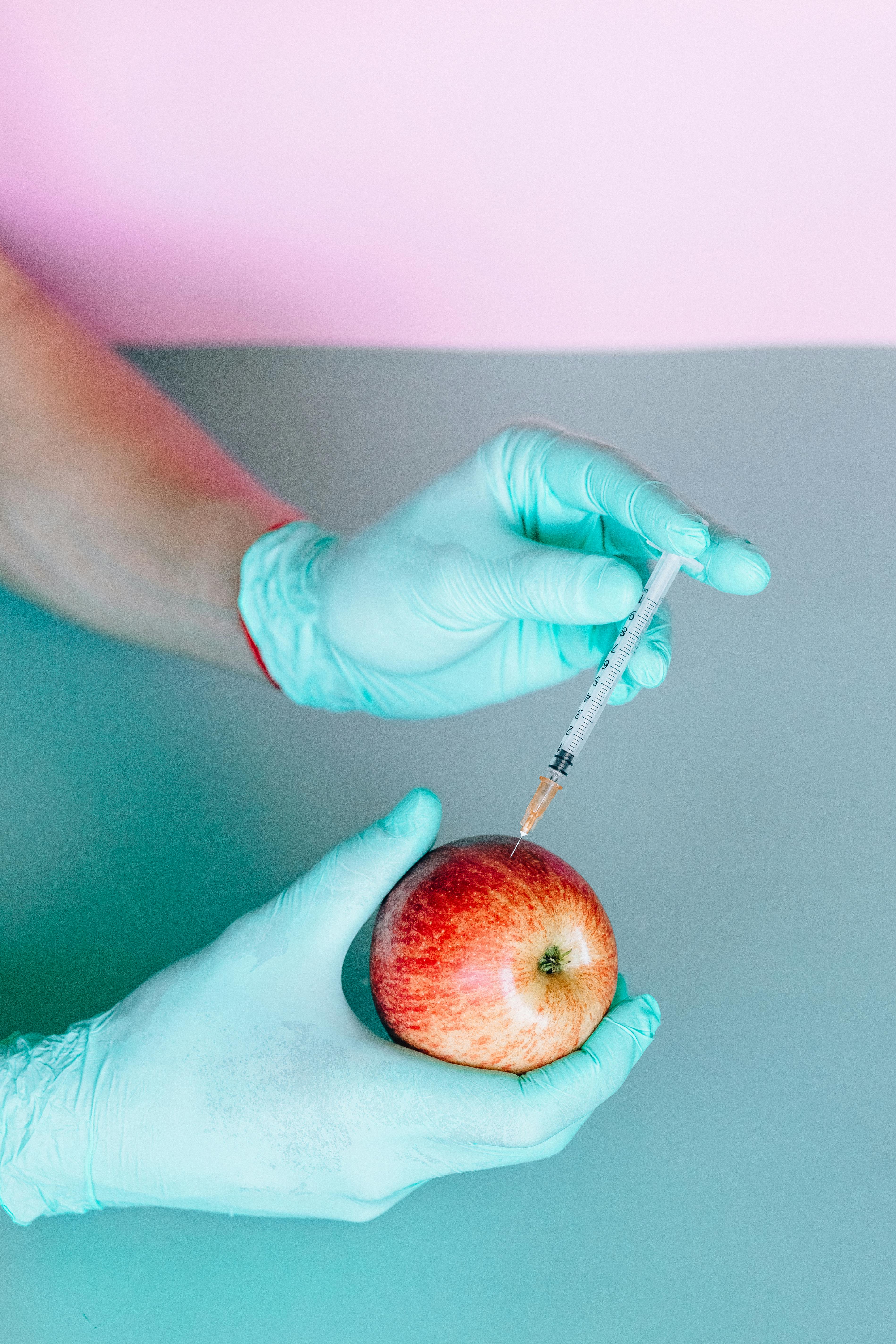 person injecting a red apple by using a syringe