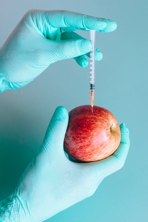 Free Person Injecting a Red Apple by Using a Syringe Stock Photo