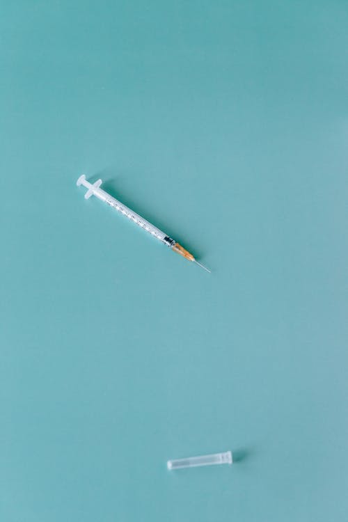 Free An Uncapped Syringe on Teal Background Stock Photo