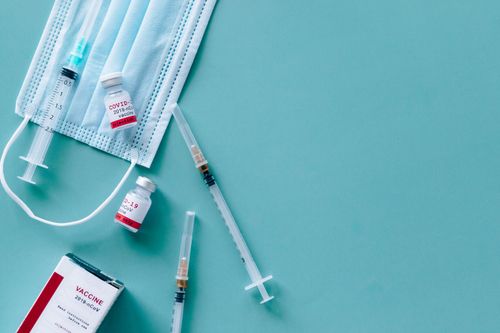 Free Face mask, syringes, and COVID-19 vaccine vials against blue background. Stock Photo