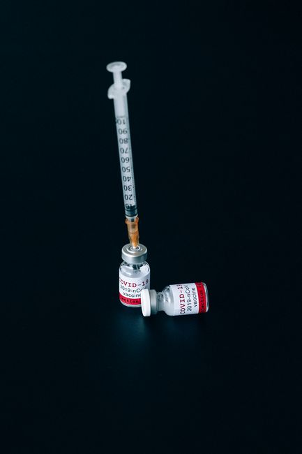 A close-up of COVID-19 vaccine vials and a syringe on a dark background, emphasizing vaccination efforts.