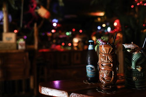 Beer Bottle and Ceramic Tiki Mugs on Wooden Table