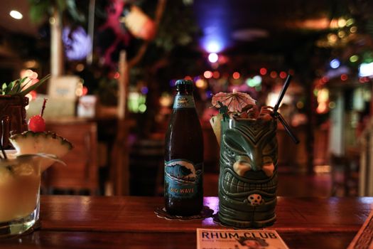 A tiki-themed bar setting with a Big Wave beer and creative cocktails on a wooden counter.