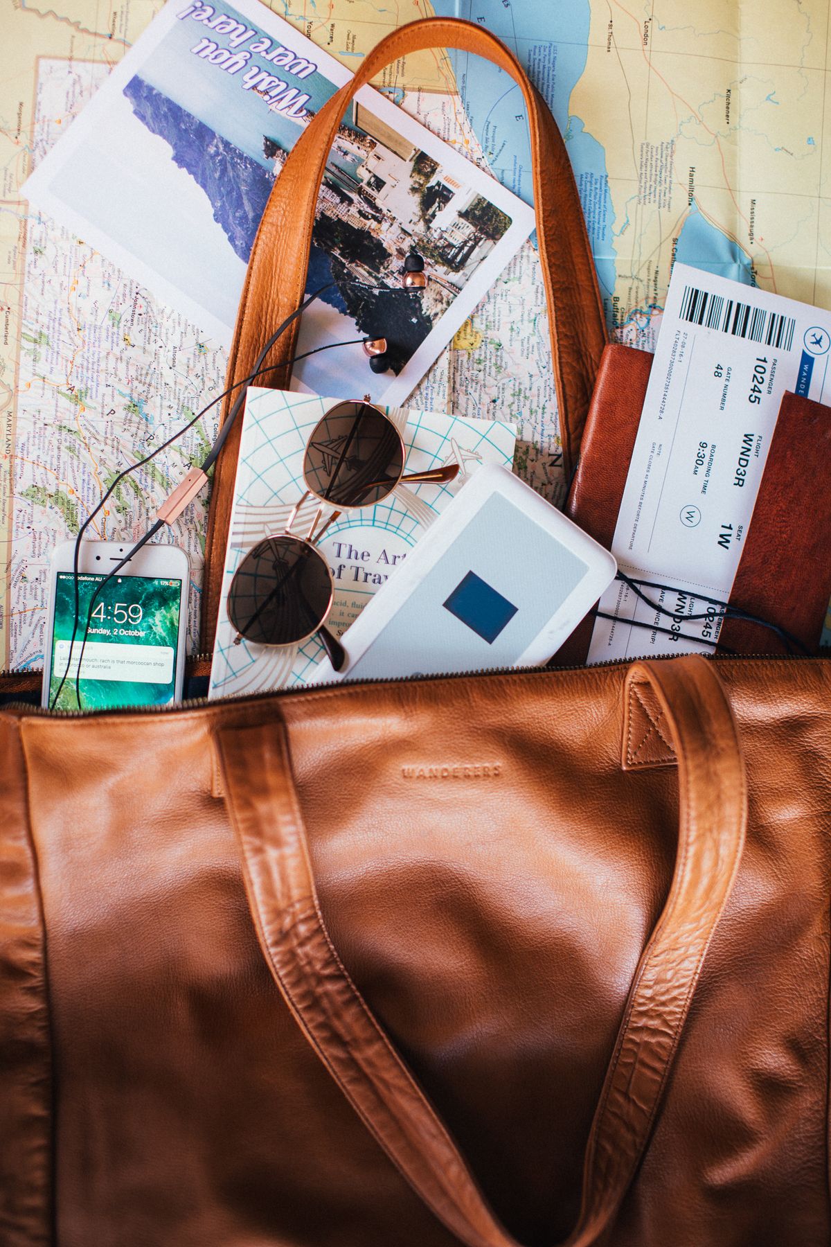 Travel bag arranged with maps, tickets, sunglasses and journal