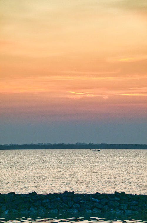Free Small boat floating on rippling water of wavy sea against cloudy sunset sky Stock Photo