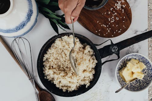 Free Overhead view of rice being cooked in a frying pan with butter and utensils. Stock Photo
