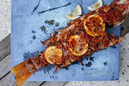Free A perfectly grilled fish garnished with lemon slices served on a blue platter. Stock Photo