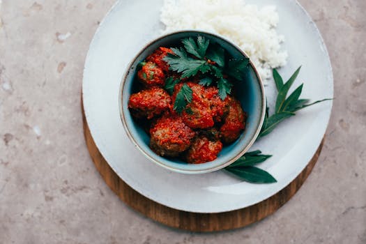 Top view of meatballs in tomato sauce served with rice, garnished with fresh herbs.