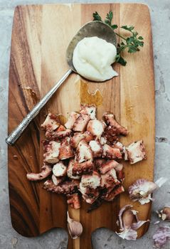 Delicious chopped octopus with aioli and garlic on a wooden board, top view.