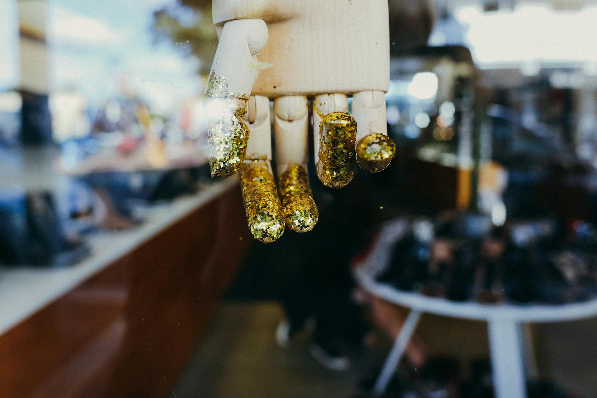 A mannequin hand with golden glitter, reflected in a shop window.